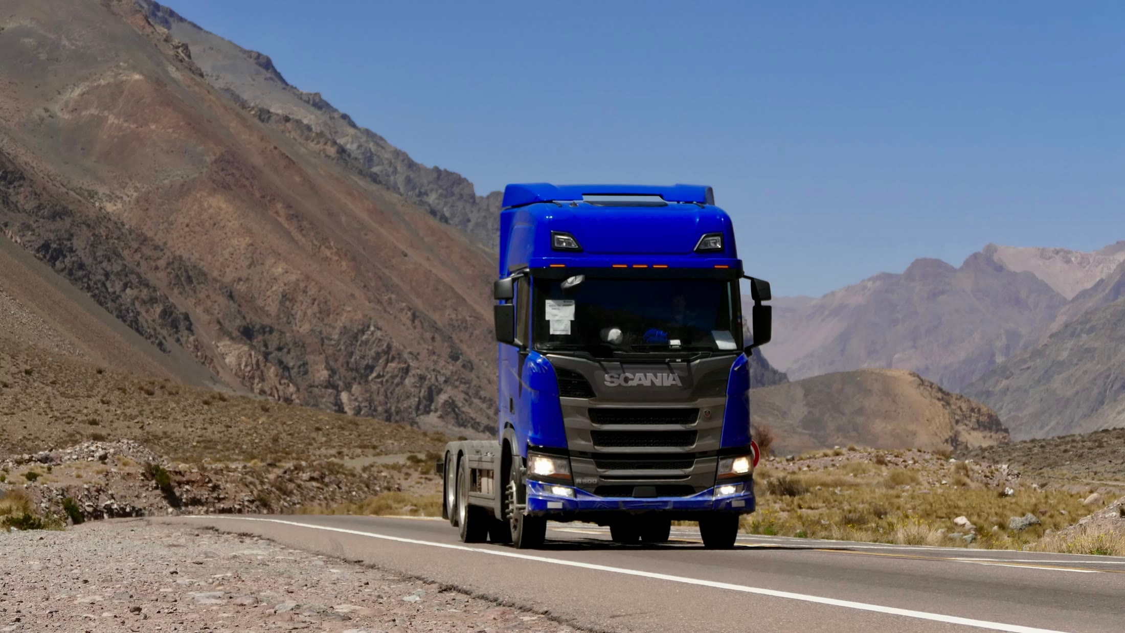 Blue Scania truck driving through a mountain landscape
